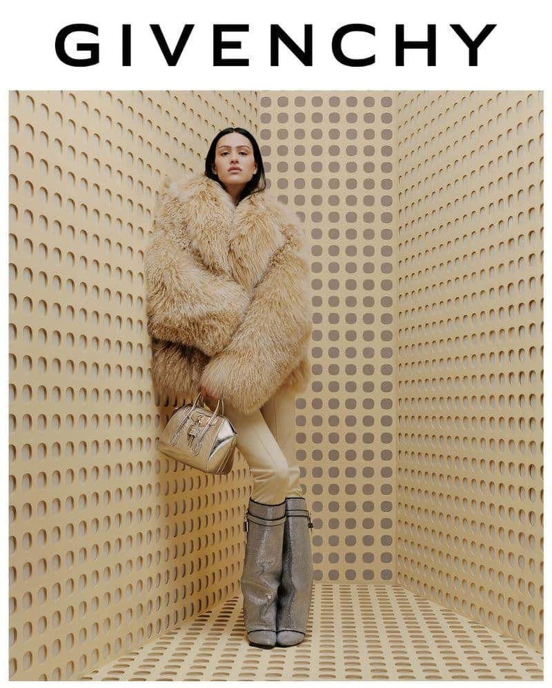 Fashion shot of a woman wearing a fur coat, metallic boots, and carrying a handbag, posed in a geometric patterned photo studio.