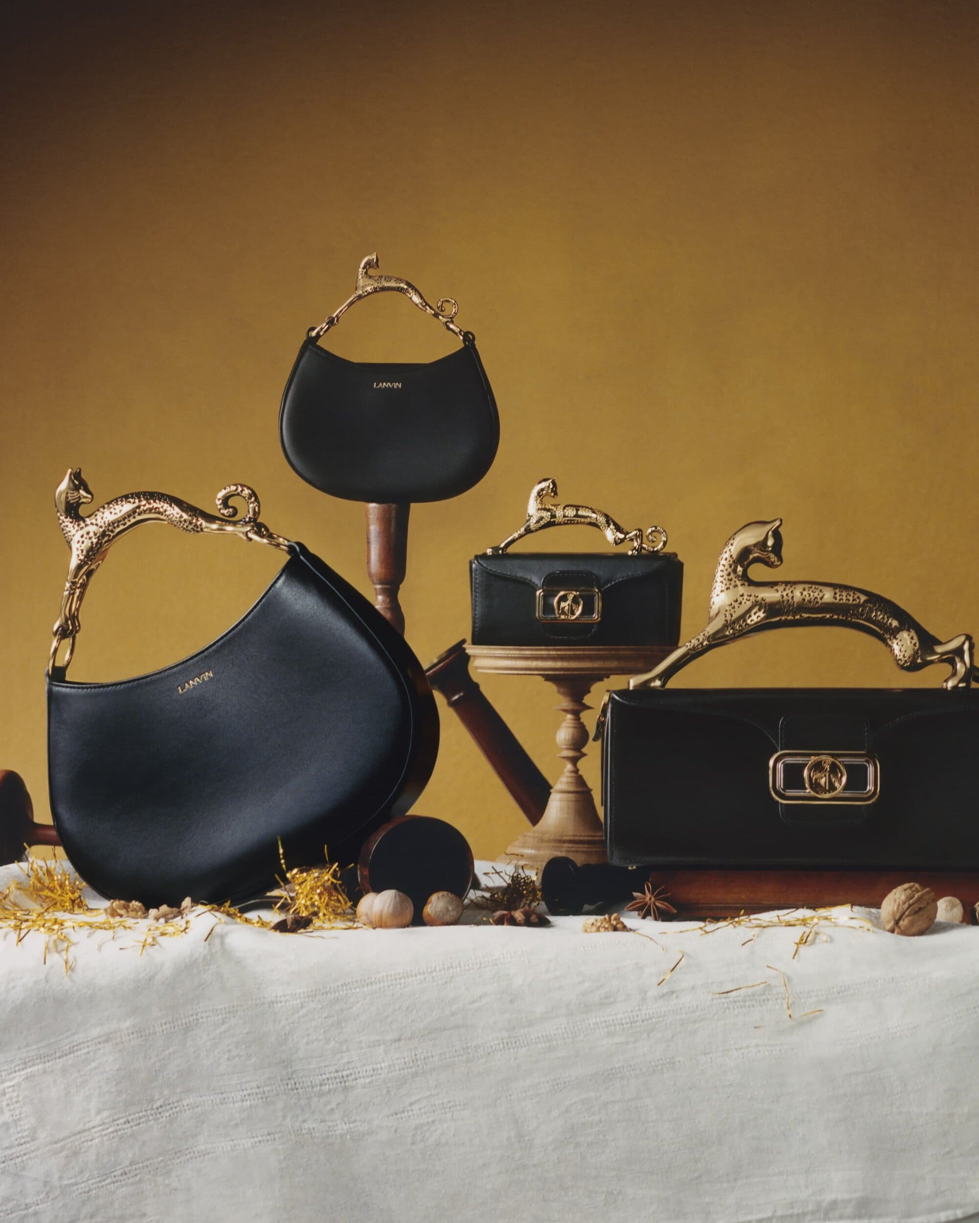 Arrangement of Lanvin handbags in black leather with ornate golden handles, on display with nuts and dried foliage, studio shot.