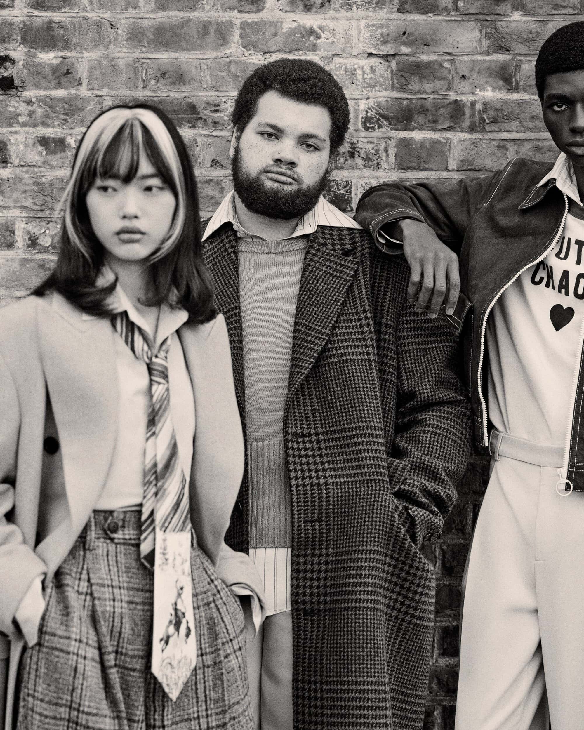 Three fashion models pose against a brick wall. The model on the right wears a 'Youth Chaos' shirt. The image is in black and white.