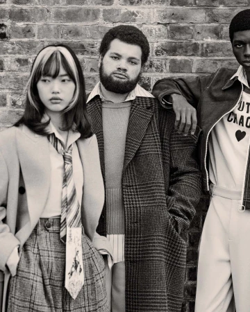 Three fashion models pose against a brick wall. The model on the right wears a 'Youth Chaos' shirt. The image is in black and white.