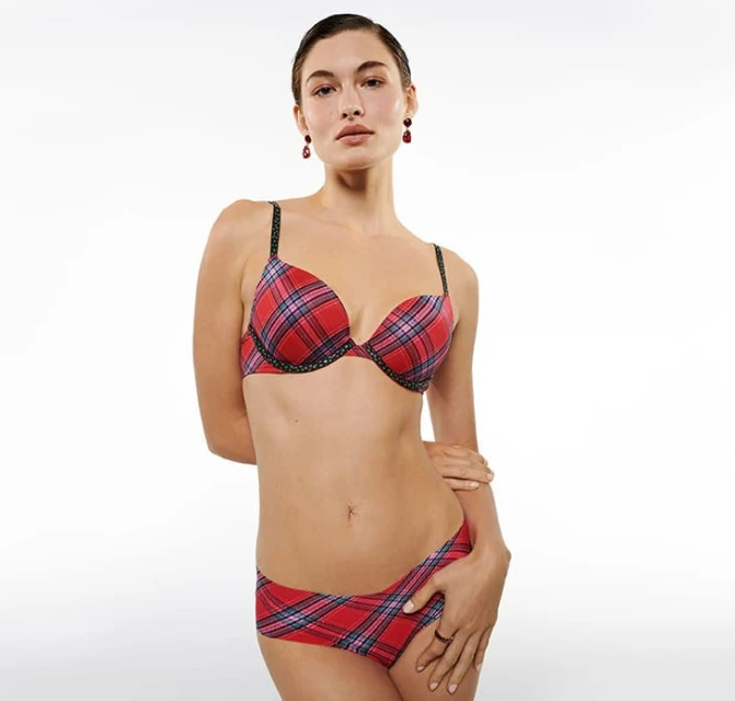 Woman in red plaid bra and underwear set stands against a white backdrop. Studio lighting, clean aesthetic. Fashion editorial style.