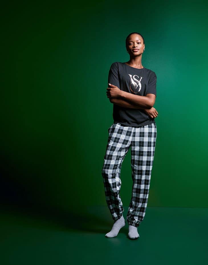 Full-length studio shot of an adult female wearing a t-shirt, plaid pants, and socks against a graduated green background.