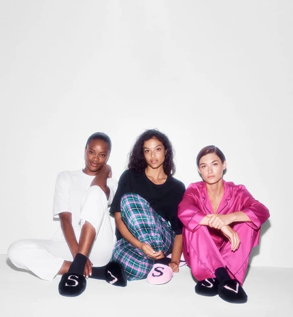 Three women sit in a studio wearing fashionable loungewear and slippers. The backdrop is a bright white, creating a clean, modern look.