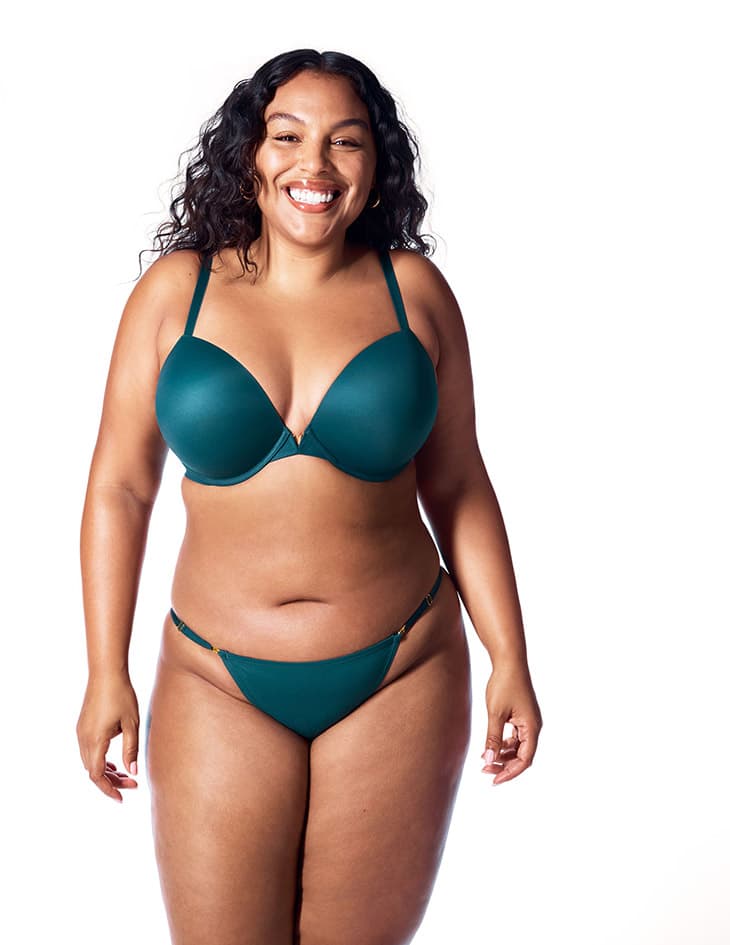 Smiling woman in a teal lingerie set posing against a white background, showcasing a positive body image and confidence.