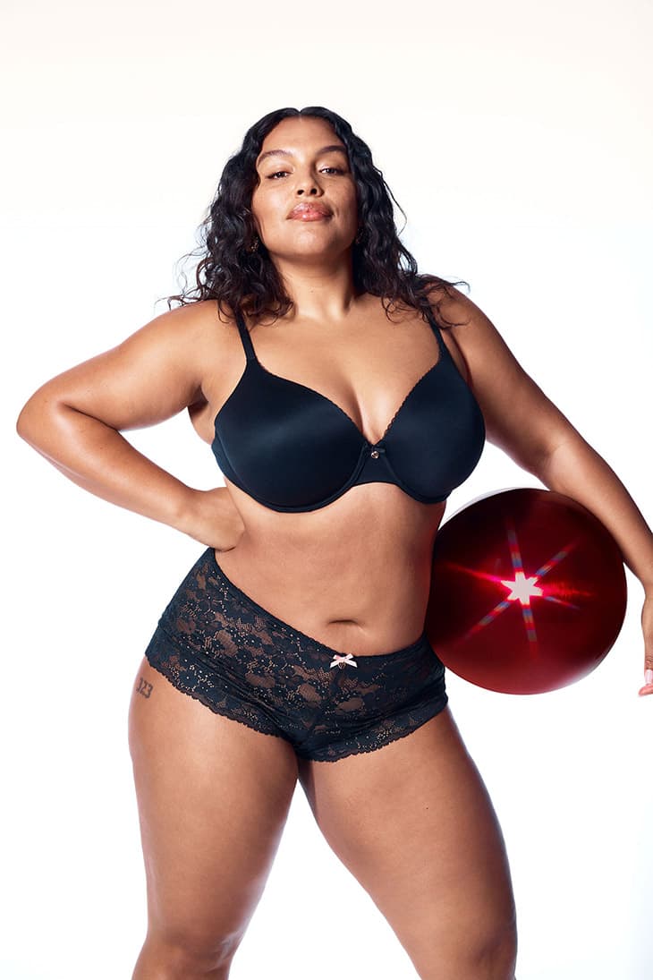 Adult female model in lingerie poses in a studio with a prop. Fashion advertisement featuring a black bra and boy-short underwear.