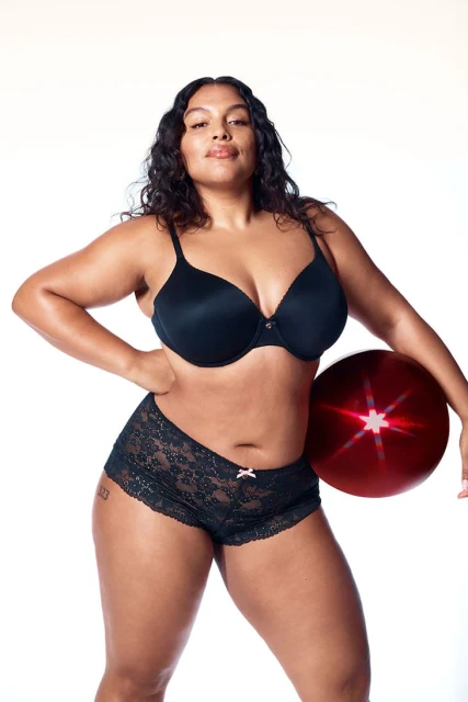 Adult female model in lingerie poses in a studio with a prop. Fashion advertisement featuring a black bra and boy-short underwear.