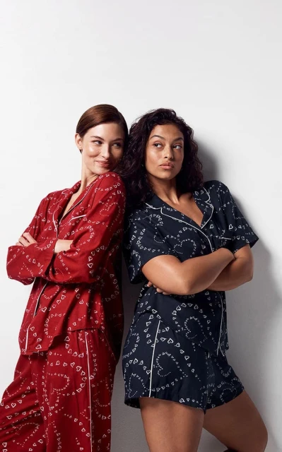 Two adult females in matching patterned pajamas pose back-to-back against a white wall in a studio with soft lighting.