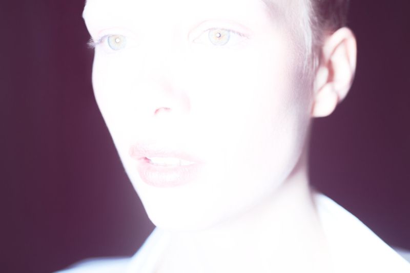 Close-up portrait of a woman with fair skin, green eyes, and short hair against a dark background. High key photography.