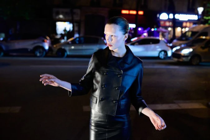 Fashionable woman in leather jacket and skirt standing on city street at night with cars in background. Dark and edgy fashion shoot.