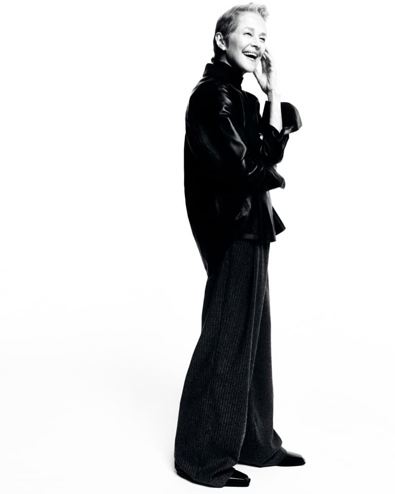 Full-length black and white portrait of a mature adult woman smiling, wearing a dark top and dark pants in a white photo studio.