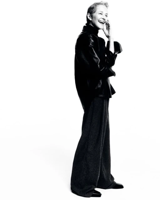 Full-length black and white portrait of a mature adult woman smiling, wearing a dark top and dark pants in a white photo studio.