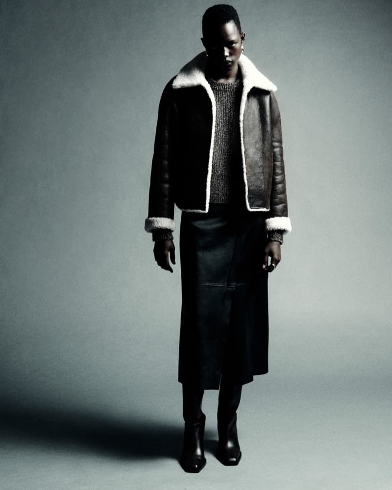 Fashionable portrait of an African woman in a leather aviator jacket with fur collar, grey knit sweater, leather skirt, and boots in a studio setting.