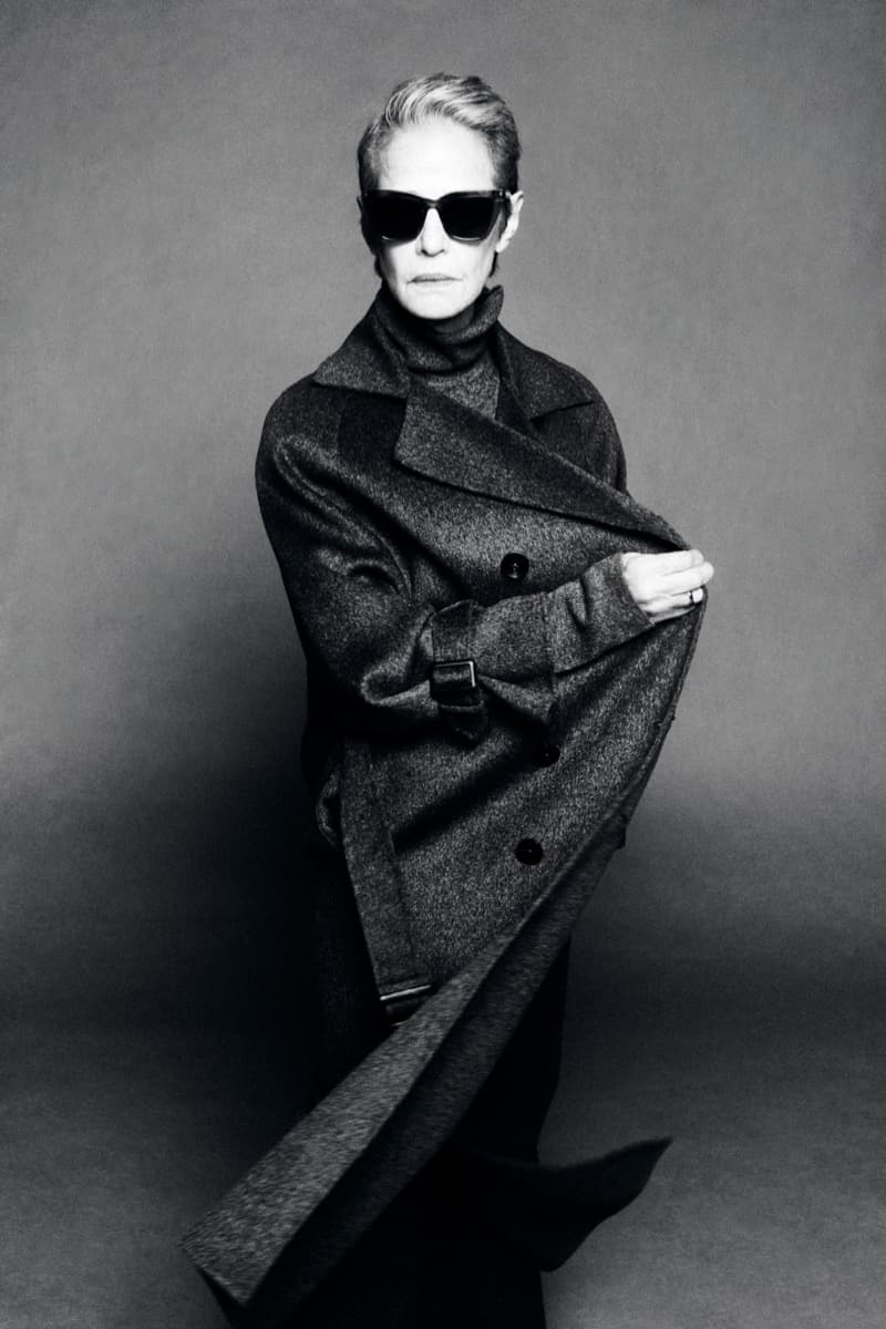 Charlotte Rampling wearing dark sunglasses and a draped charcoal wool coat over a turtleneck in black and white.