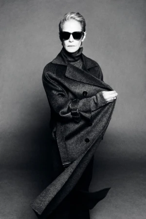 Charlotte Rampling wearing dark sunglasses and a draped charcoal wool coat over a turtleneck in black and white.