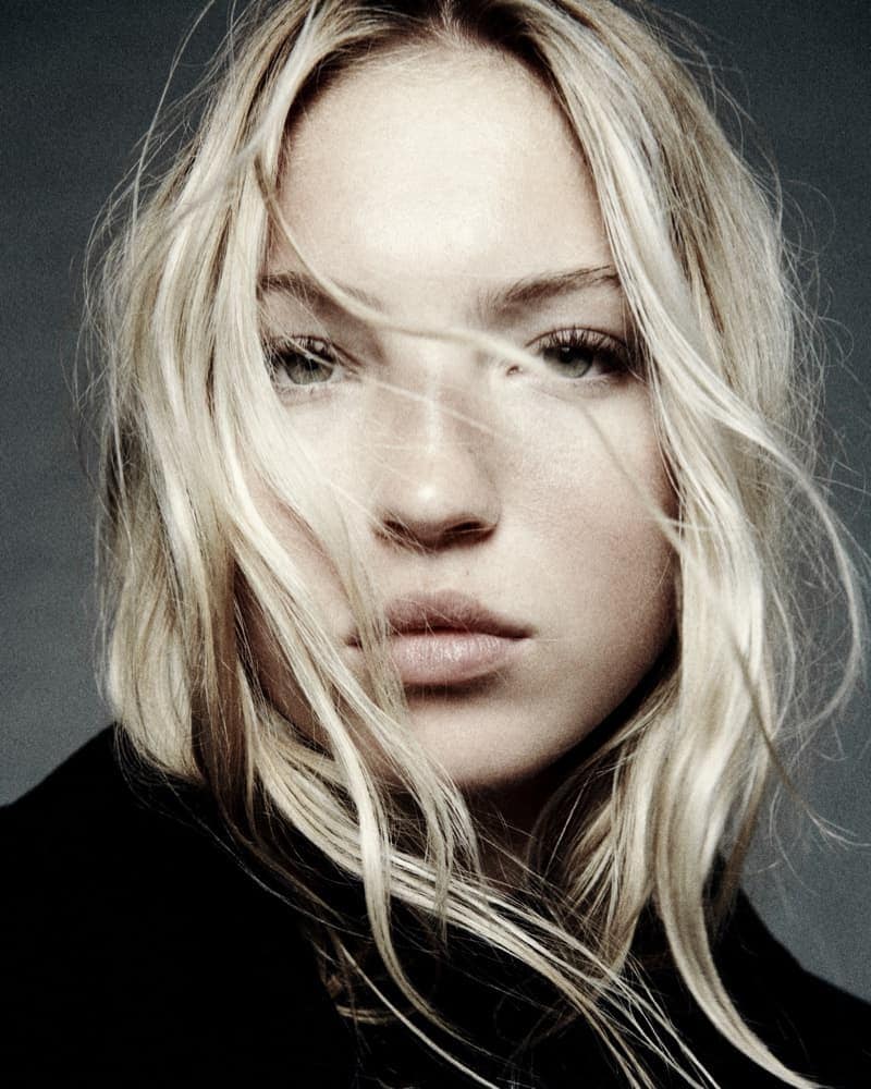 Close-up portrait of a blonde woman with light eyes, featuring soft lighting, neutral colors, and a shallow depth of field.