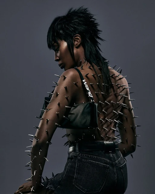 Fashionable woman with dark hair and exposed back decorated with metal spikes, wearing dark jeans and a black shoulder bag. 