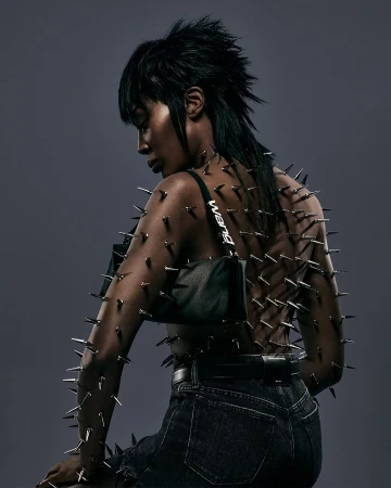 Fashionable woman with dark hair and exposed back decorated with metal spikes, wearing dark jeans and a black shoulder bag. 