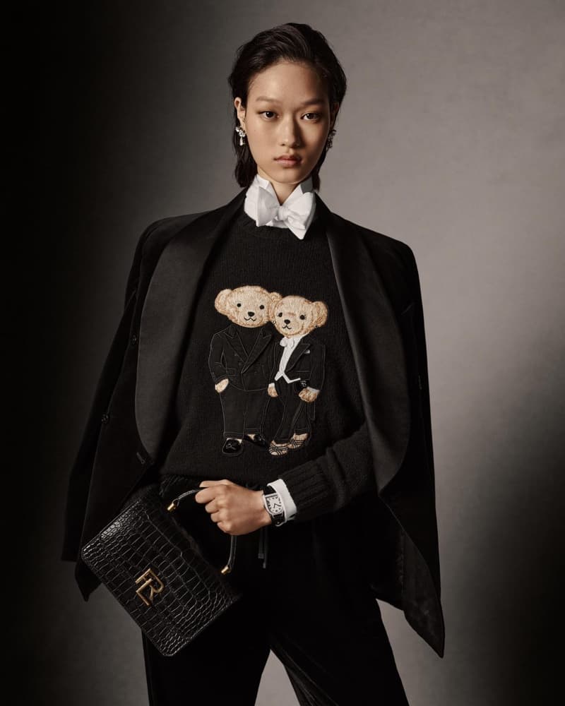 Portrait of an Asian woman in black blazer, black sweater with teddy bear design, and black pants, holding a black purse.
