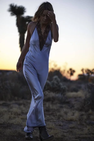 A woman in a light blue dress walks through the desert landscape at sunset, a Joshua tree visible in the background.
