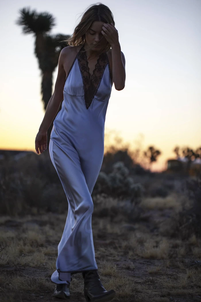 Model in a long silk slip dress with lace trim walking outdoors at sunset with desert vegetation in the background.