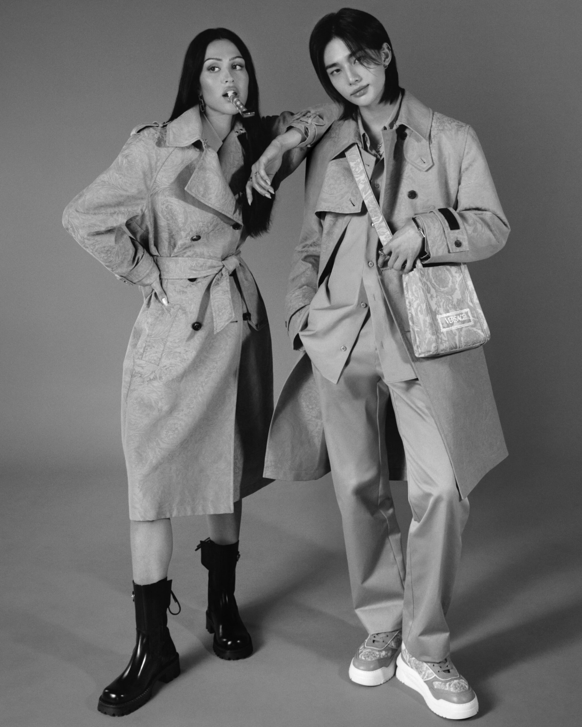 A stylish black and white portrait of a woman and man in matching patterned trench coats in a studio setting, showcasing fashion.