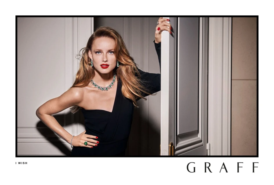 Woman in black dress wearing emerald jewelry poses in doorway. Fashion shot. Glamorous portrait, indoor setting, luxury jewelry ad.