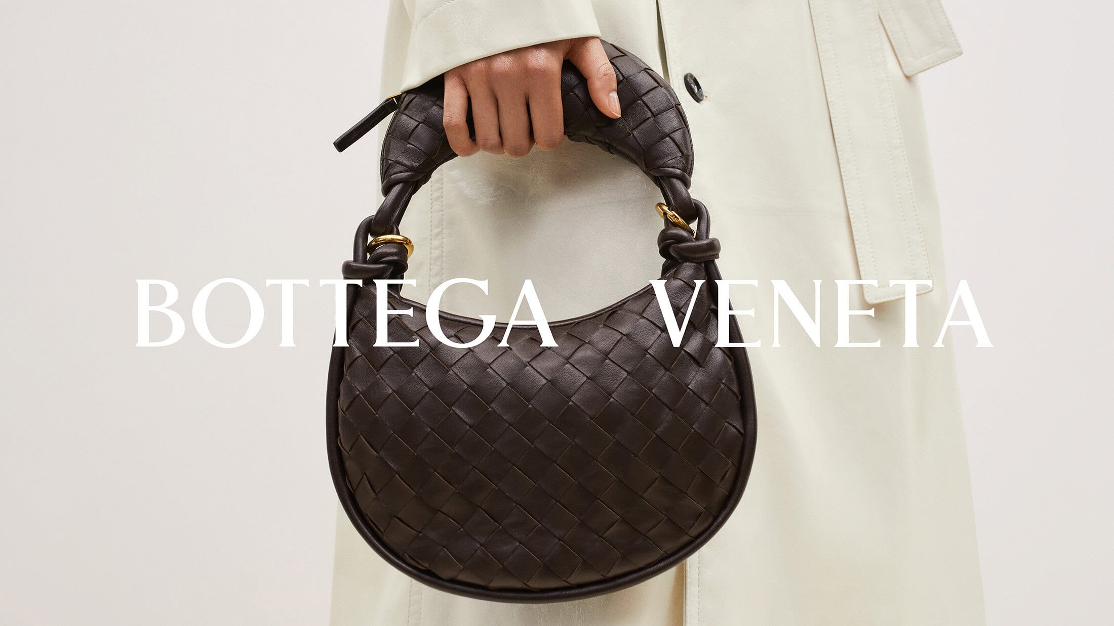 Bottega Veneta brown woven leather handbag carried by a person in a studio setting with a neutral-colored coat.