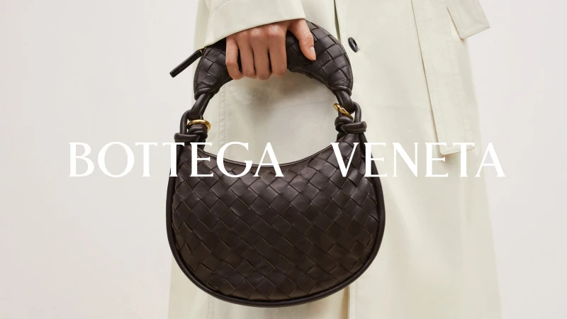 Bottega Veneta brown woven leather handbag carried by a person in a studio setting with a neutral-colored coat.