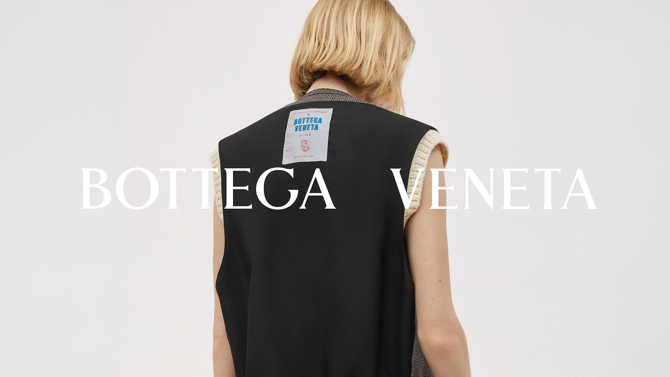 Fashion shot of a woman wearing a black vest with cream trim, posing in front of a neutral background, with a Bottega Veneta logo.