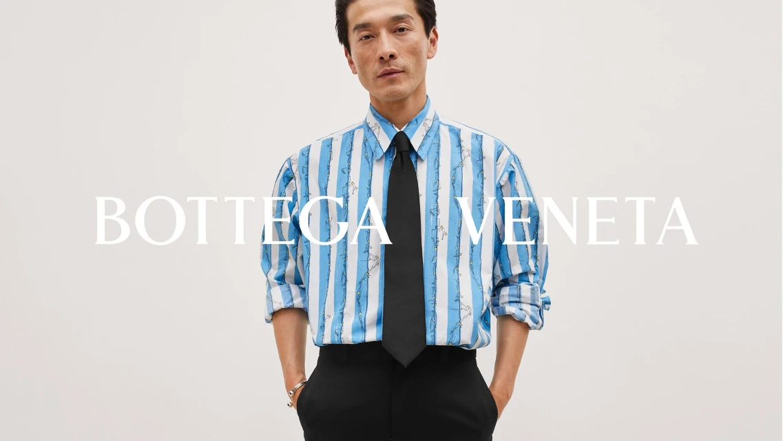 An Asian adult male model poses in a light blue striped shirt with a black tie and black trousers against a plain neutral background.