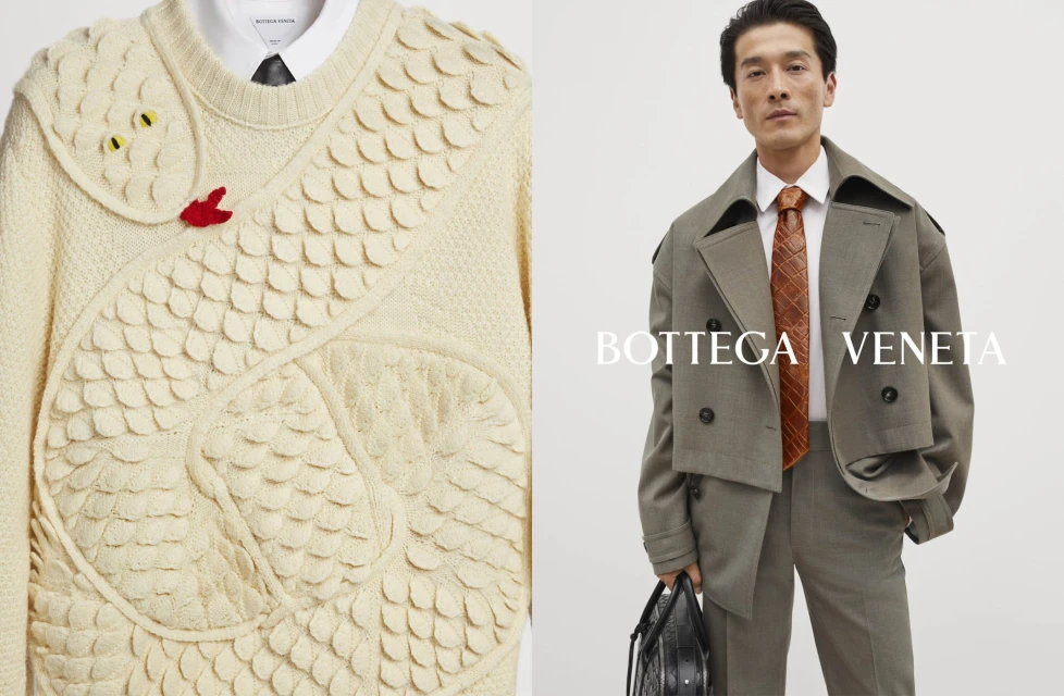 Fashion editorial shot showcasing a man in a grey suit with an orange tie and a sweater featuring a snake design against a clean backdrop.
