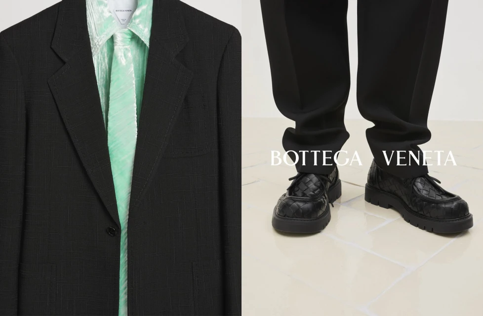 Close-up on a black blazer with a light green shirt and tie, paired with black trousers and leather shoes; Bottega Veneta logo.
