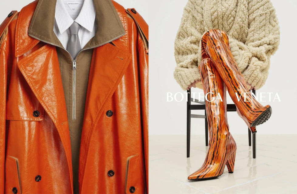 Fashion still life featuring an orange patent leather trench coat and matching tiger-print thigh-high heeled boots and a tan sweater.
