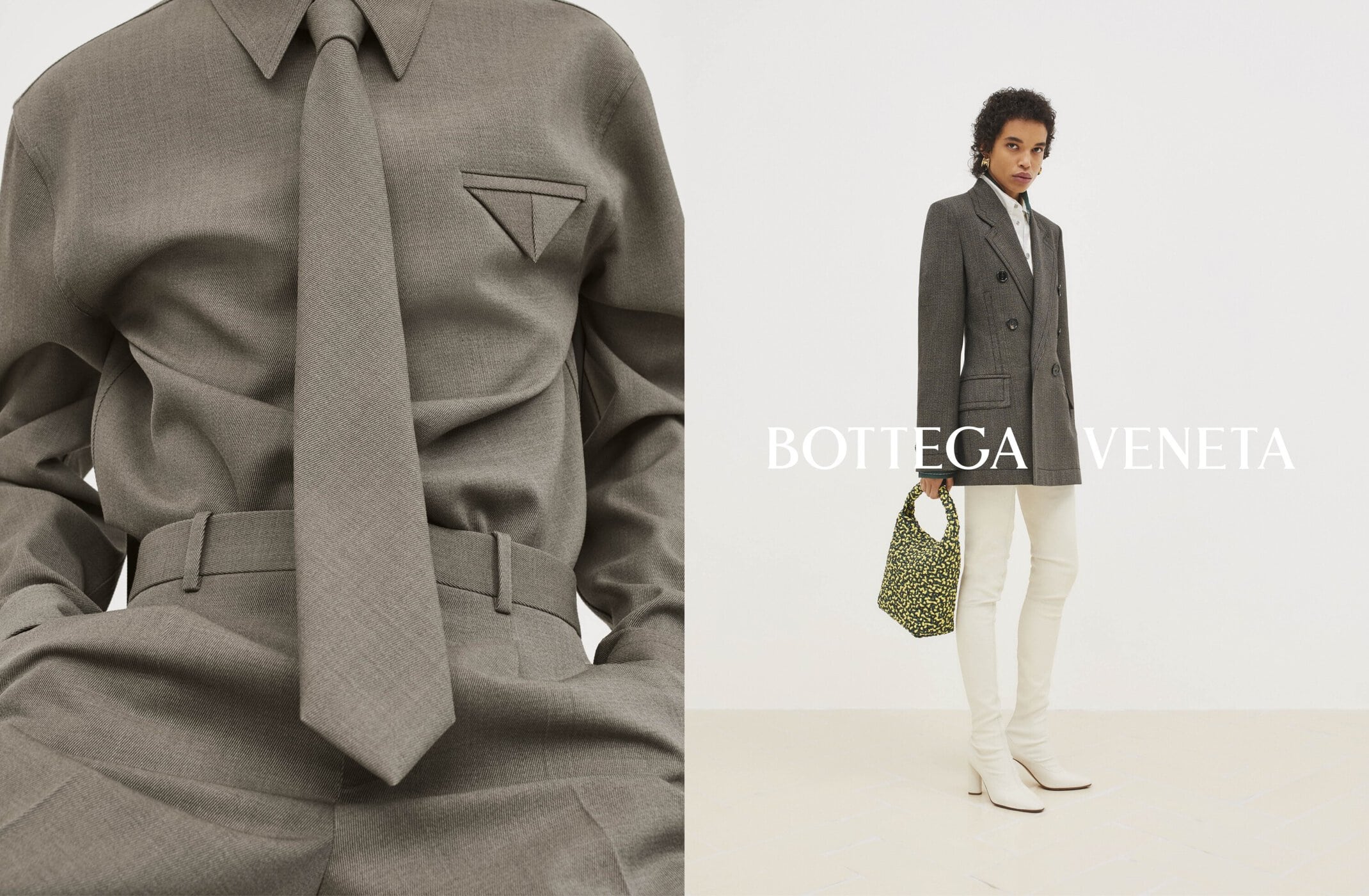 Fashion editorial featuring an adult female model wearing a grey tailored shirt, tie, blazer, and cream-colored pants in a studio.