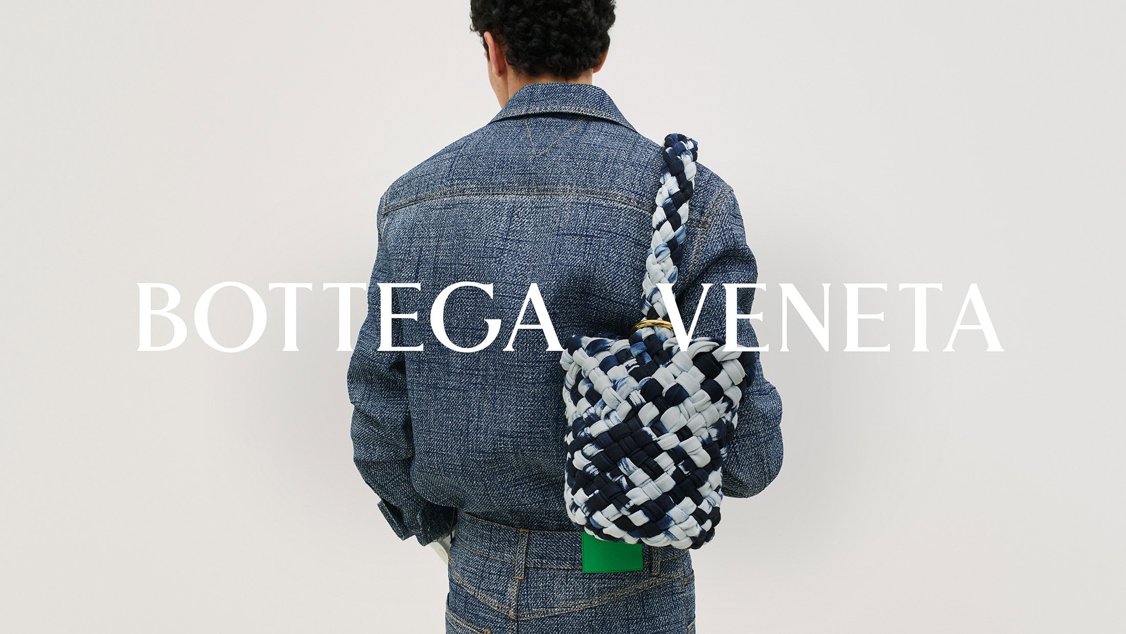 A person wears a denim jacket and pants with a woven bucket bag in front of a white background, with the brand name overlaid.
