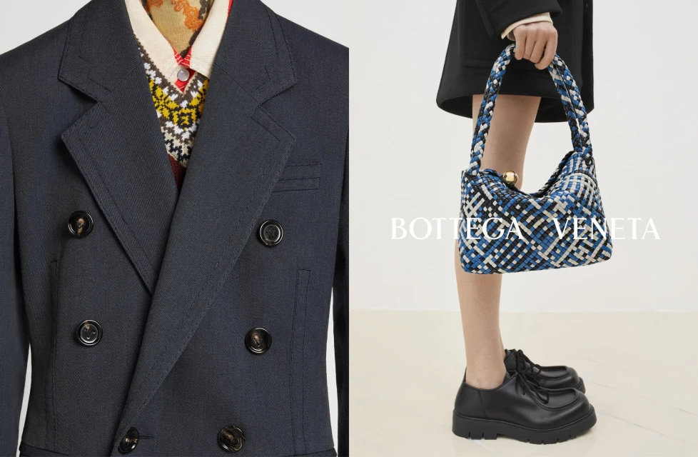 Fashion editorial shot of a double-breasted navy blazer with a patterned sweater and woman carrying a blue woven purse with black loafers.