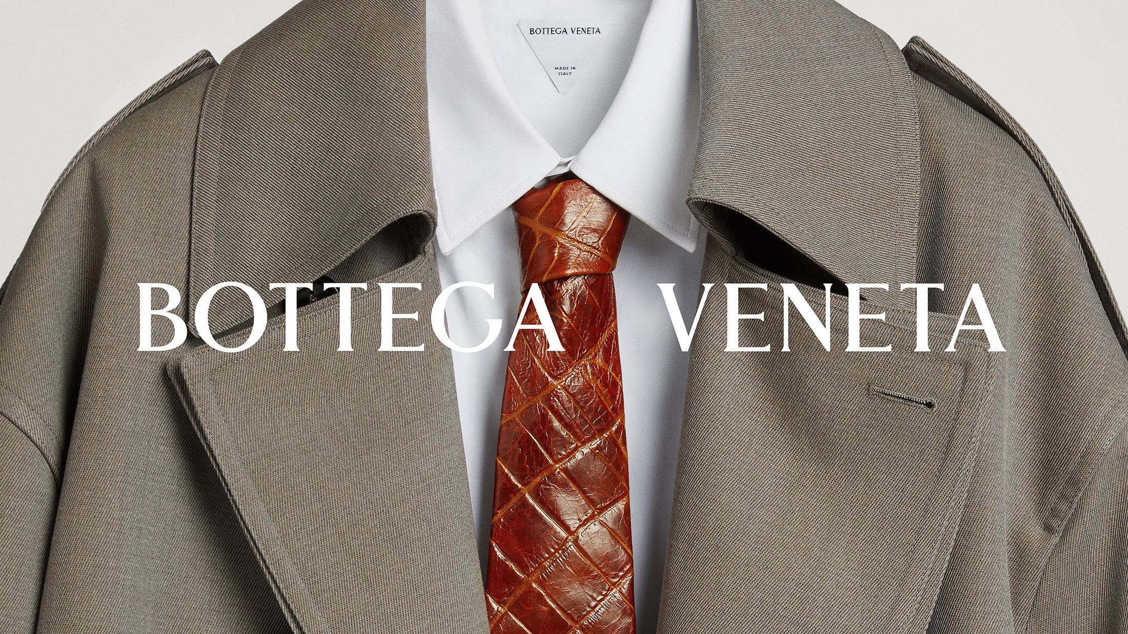 Tan trench coat, white collared shirt, and brown woven tie on a neutral background, displaying fashion apparel in a studio setting.