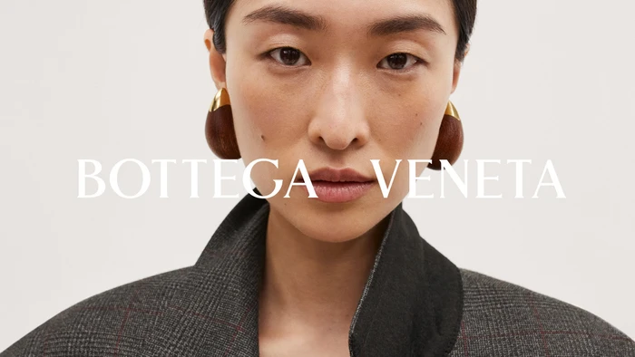 Close-up portrait of model Chu Wong wearing large wooden drop earrings and a grey plaid jacket for Bottega Veneta.