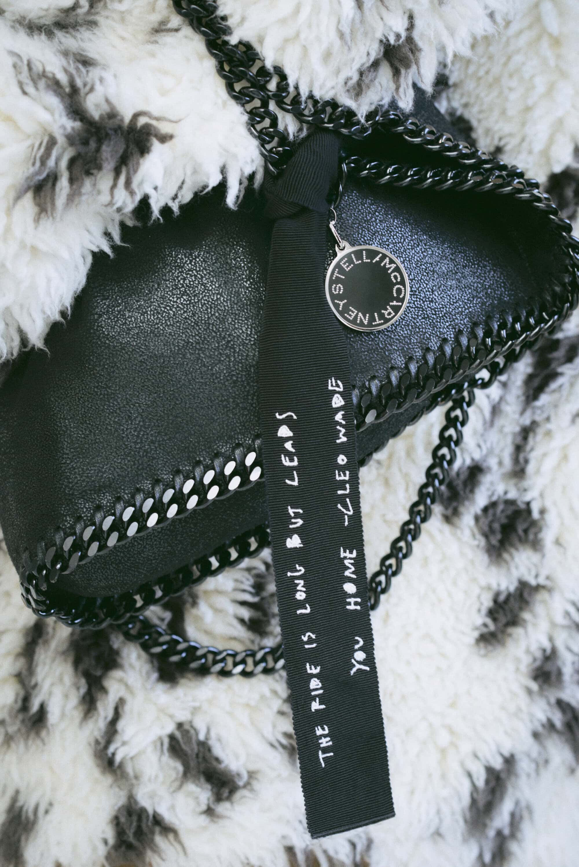 Black Stella McCartney handbag with chain strap and branded tag on an animal print faux fur throw, fashion product shot.