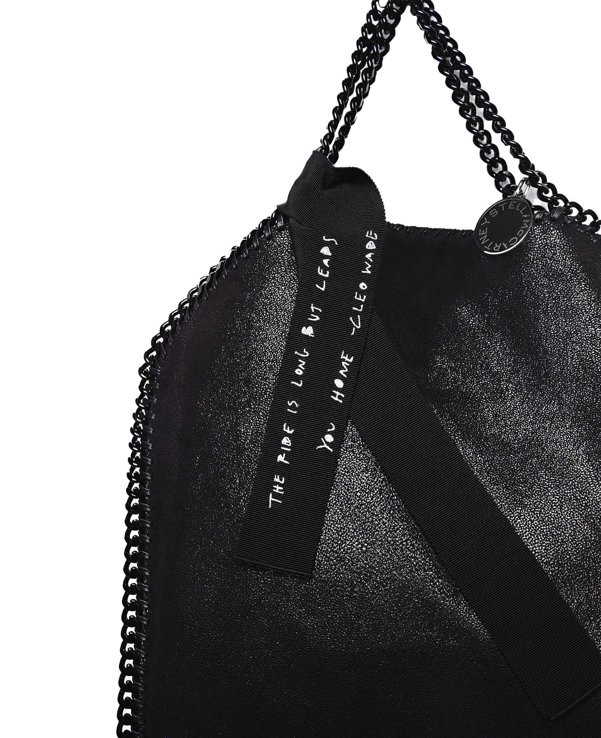 Black Stella McCartney tote bag with chain straps and a ribbon accent featuring a printed message, set against a clean white background.