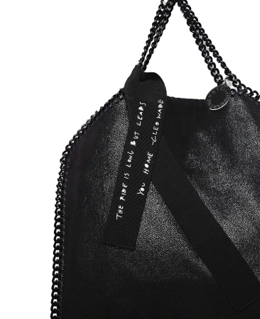 Black Stella McCartney tote bag with chain straps and a ribbon accent featuring a printed message, set against a clean white background.