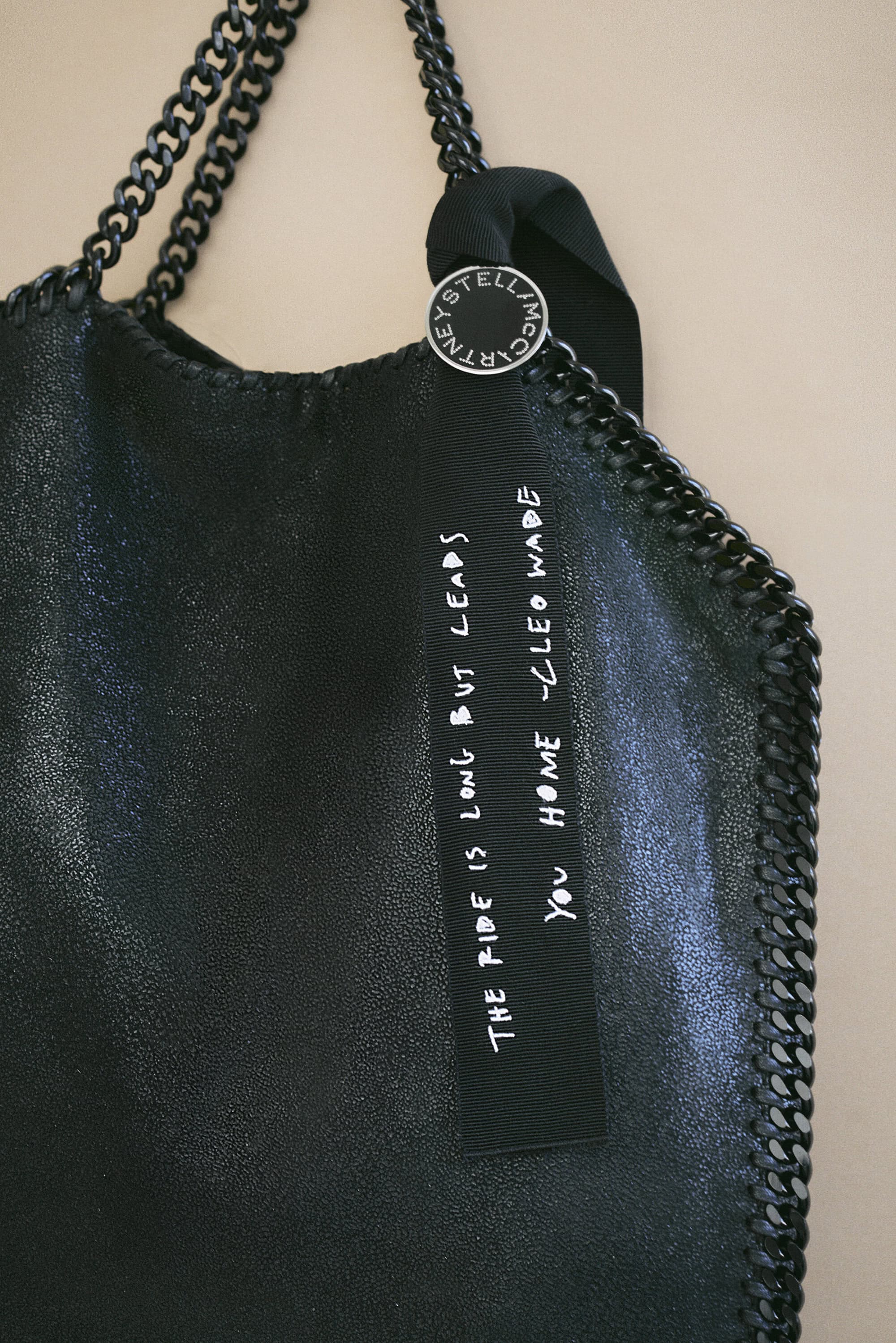 Close-up shot of a black Stella McCartney tote bag with silver chain details and a ribbon displaying white handwritten text.