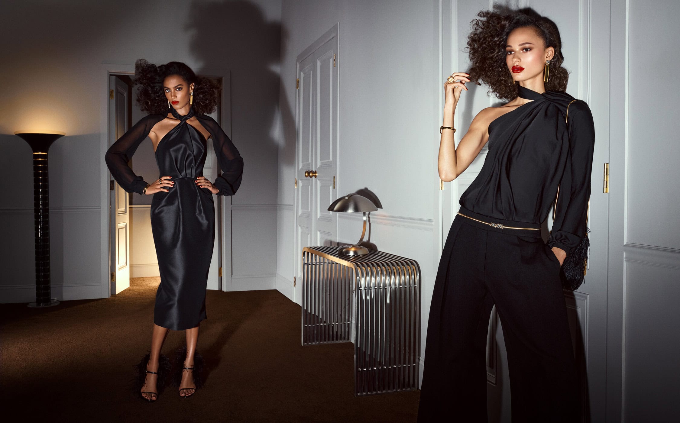 Two women showcase elegant black dresses in a minimalist studio setting with art deco-inspired props and soft lighting, creating a sophisticated fashion image.