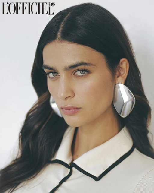 Close-up shot of a brunette female model wearing silver earrings and a white top with black trim in a photo studio setting.