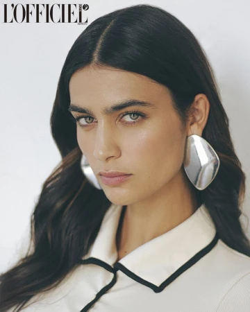Close-up shot of a brunette female model wearing silver earrings and a white top with black trim in a photo studio setting.