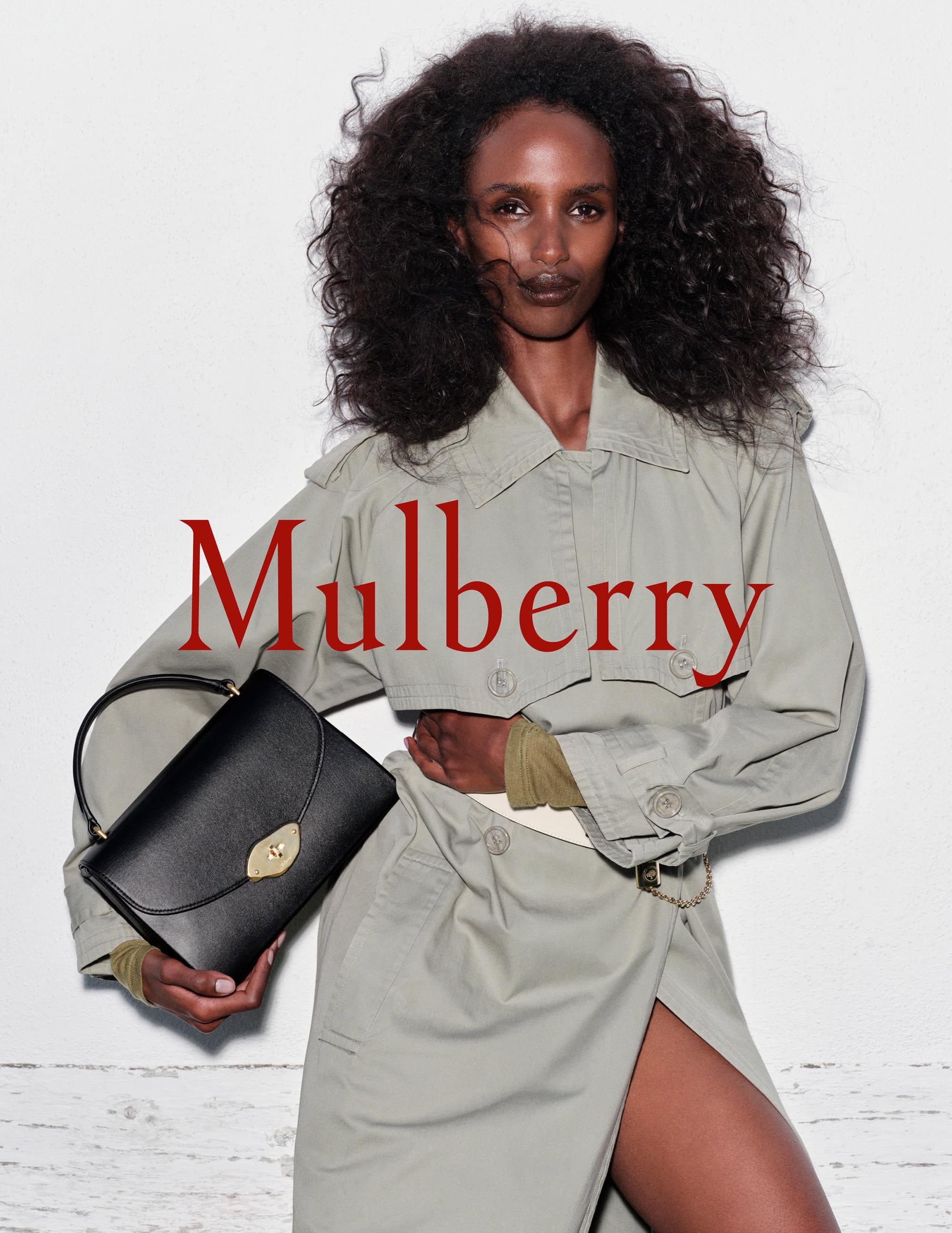 Fashion editorial featuring an African-American model holding a black leather Mulberry handbag in a studio with a white background.