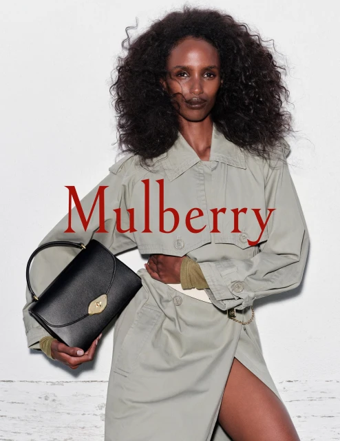 Fashion editorial featuring an African-American model holding a black leather Mulberry handbag in a studio with a white background.