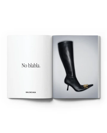 Open magazine featuring a black leather knee-high heeled boot with gold logo on a white background. Fashion editorial photography.