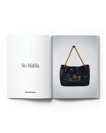 Open magazine featuring a black Balenciaga purse with a gold chain and logo against a white background, advertising the brand.