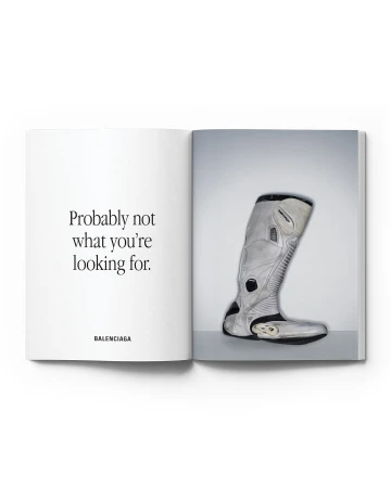 Open book with a Balenciaga advertisement featuring a grey boot on a white background with minimalist text on the opposing page.
